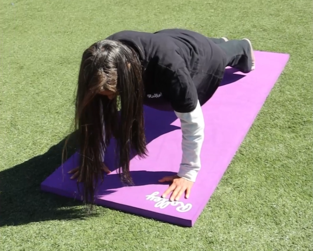 Woman doing push-ups on the magenta Rolley Classic mat on a grassy area